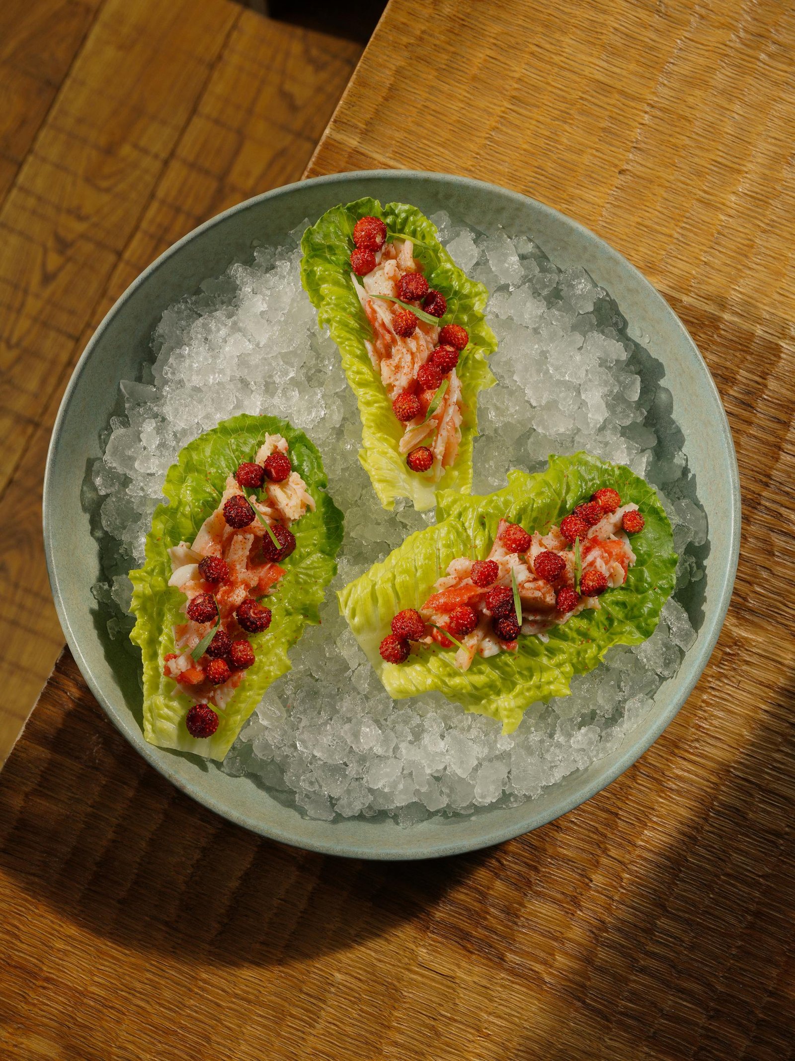 Gourmet lettuce wraps topped with fresh salmon and berries, served on crushed ice.