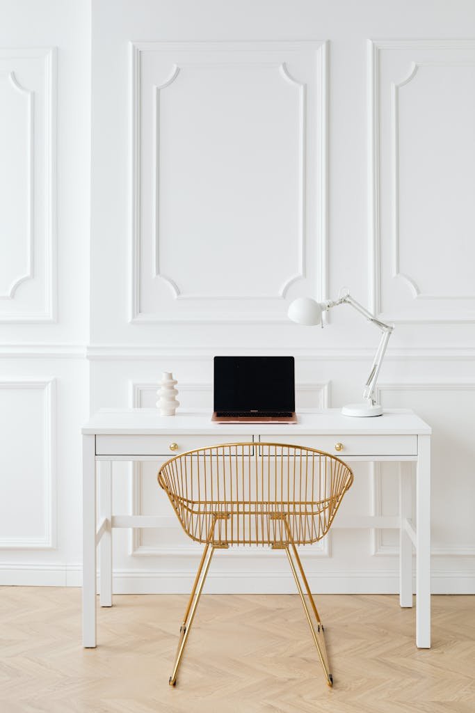 Stylish minimalist workspace with gold chair, white desk, and modern decor.