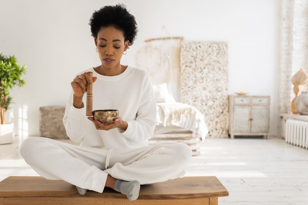 Woman practicing meditation with a Tibetan singing bowl in a serene interior setting.