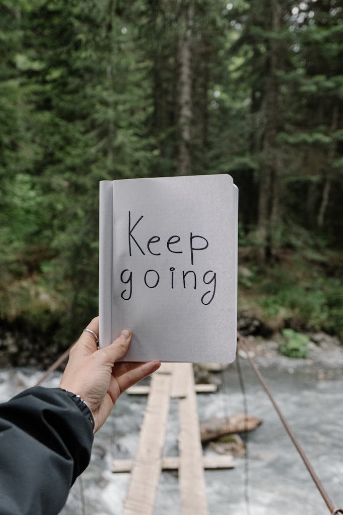 A hand holds a paper with 'Keep Going' against a forest backdrop. Nature motivation.